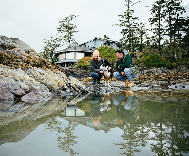 Couple with their dog crouched beside a tide pool near the Wickaninnish Inn