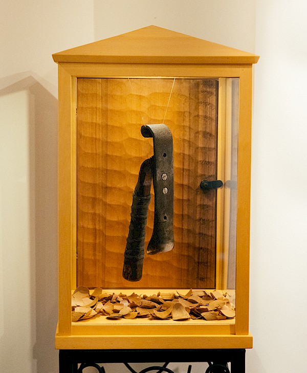 Henry Nolla’s carving adze displayed in a glass case surrounded by cedar wood chips