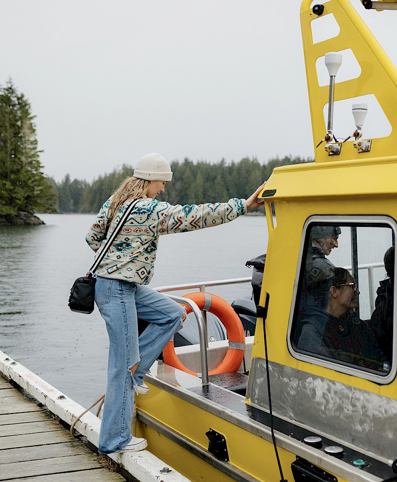 Person boarding a yellow boat at a wooden oceanside dock.