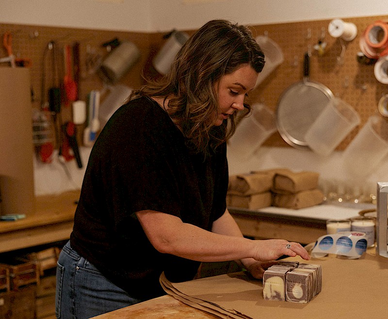 A craftsperson working carefully to package handmade soap at a well-organized workshop table, surrounded by various workshop tools and materials