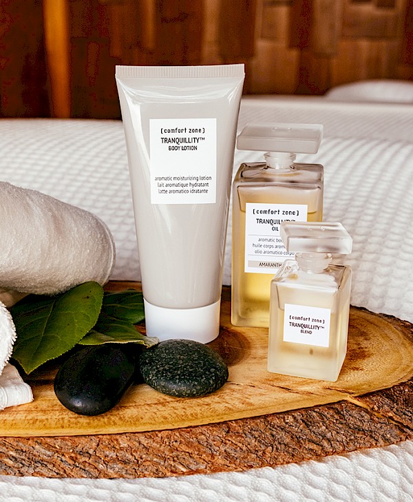 Spa products displayed on a wooden tray with stones, leaves, and towels in a cozy wooden room