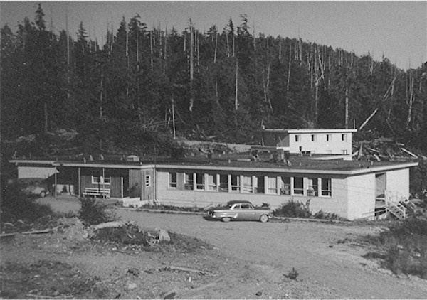 Historic black and white photograph of a vintage single-story hospital nestled in a forested area, with a classic car parked in front
