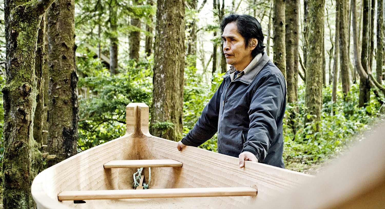 Carver Joe Martin standing beside a hand-carved cedar canoe