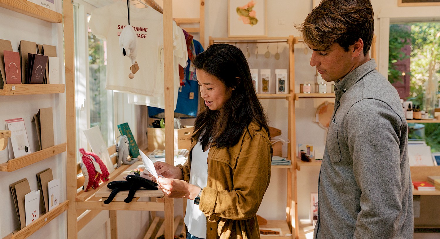 Two individuals examining products in a boutique store, surrounded by shelves of various items and clothing.