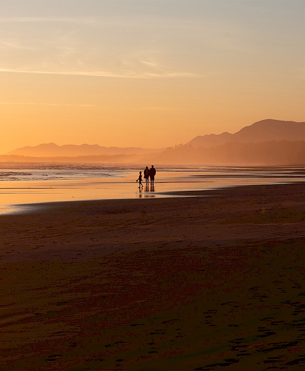 A family walking along Long Beach at sunset with mountains in the distance