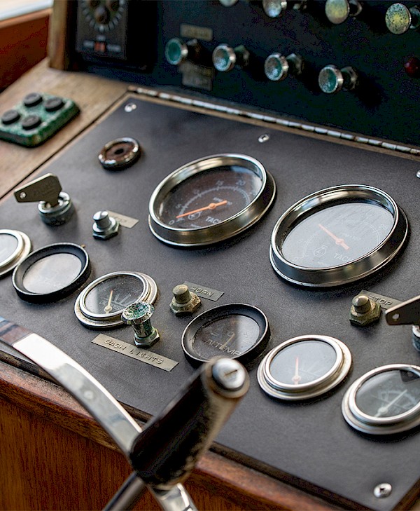 A vintage boat control panel with various gauges and dials, including levers and switches, on a wooden surface.