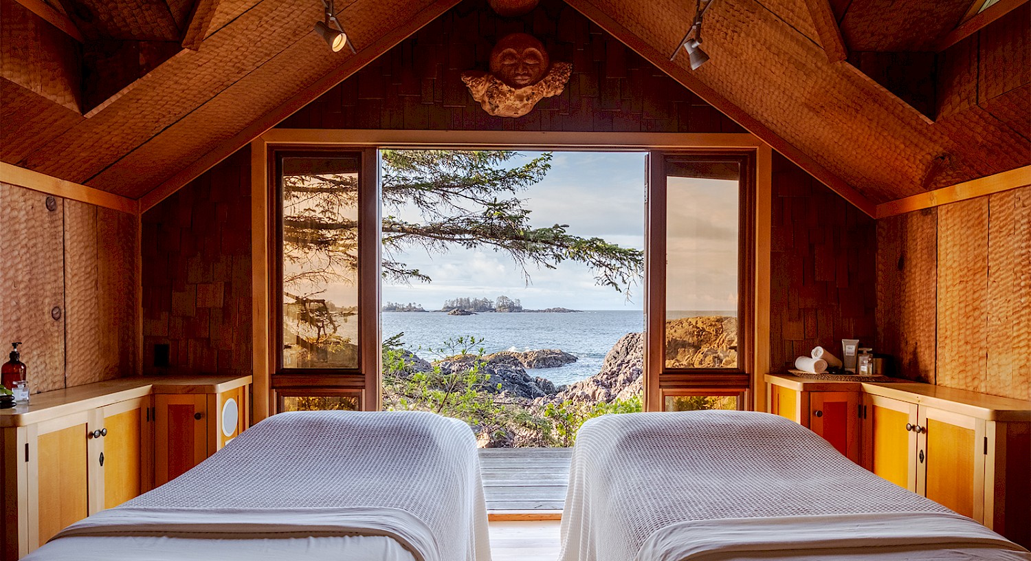 Wooden cedar massage hut at oceans edge. clean white linens on two massage tables with ocean views in background.