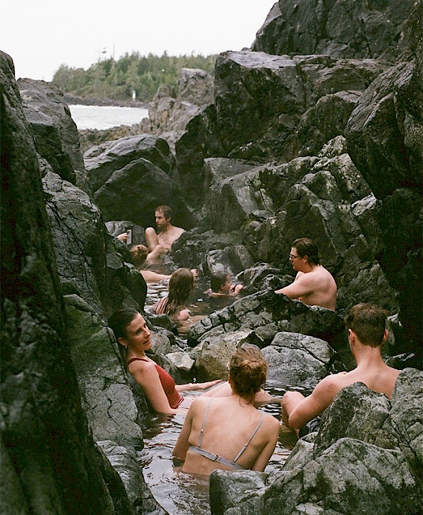 A group of people soaking in the hot springs amongst the rocks at the oceans edge